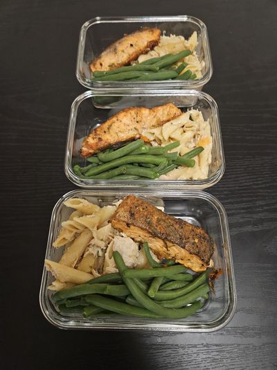 Three glass meal prep containers with salmon, green beans, and pasta.