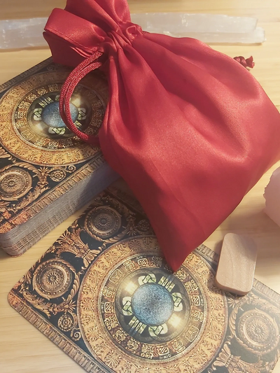 A red satin pouch on ornate tarot cards with a wooden token beside them.