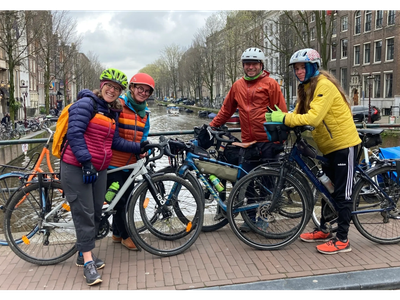 Four friends with bicycles pose on a bridge in a city canal area.