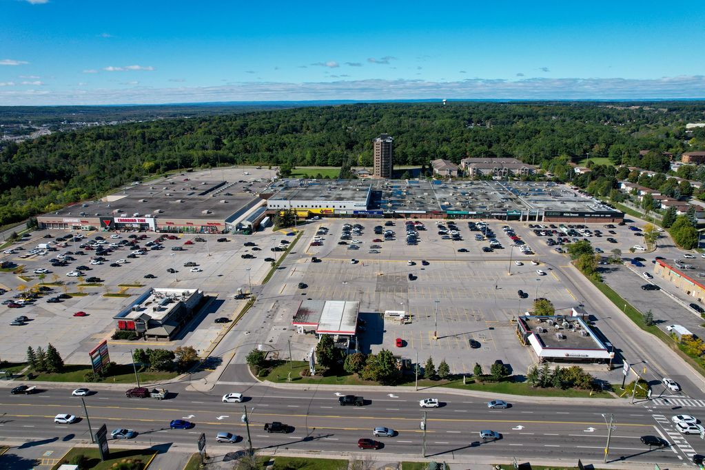 Aerial view of a shopping plaza with parking lots and surrounding greenery.