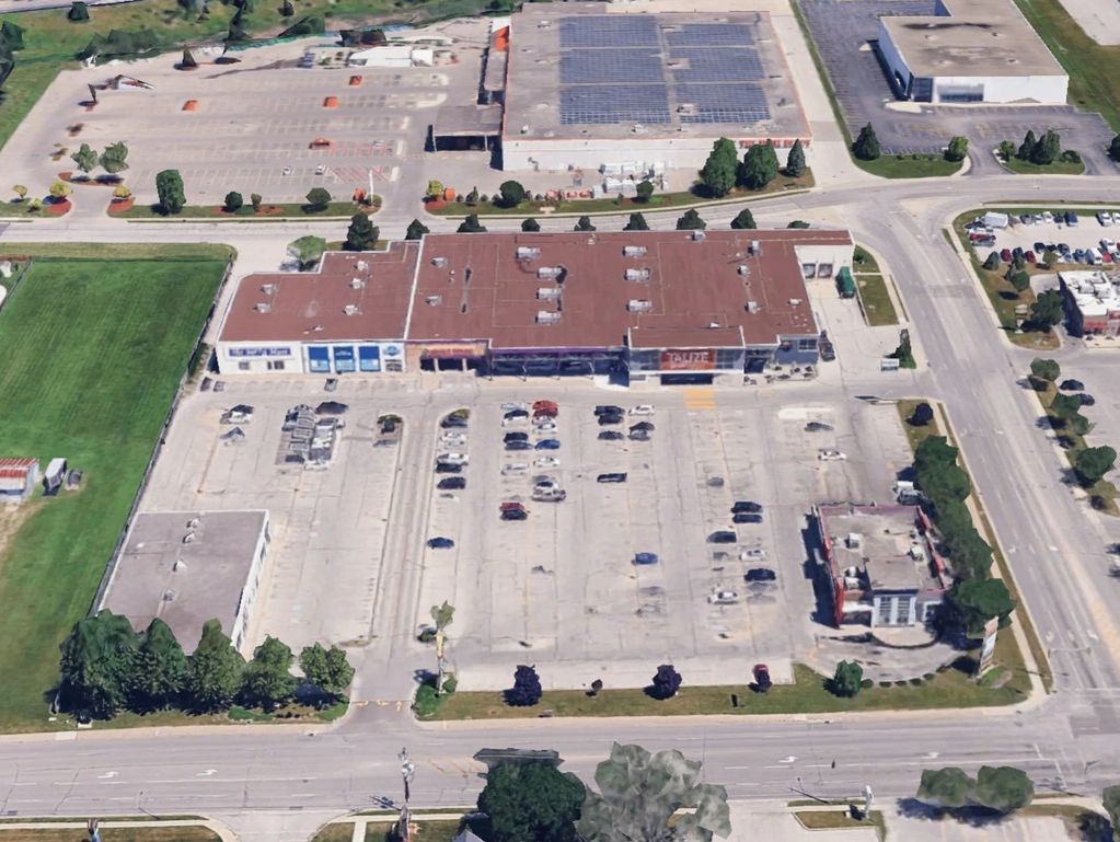 Aerial view of a shopping plaza with parking lots and surrounding roads.