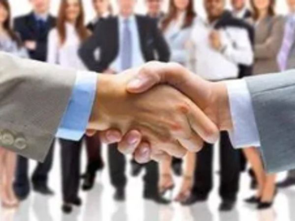 Two businesspeople shaking hands with a team in the background.