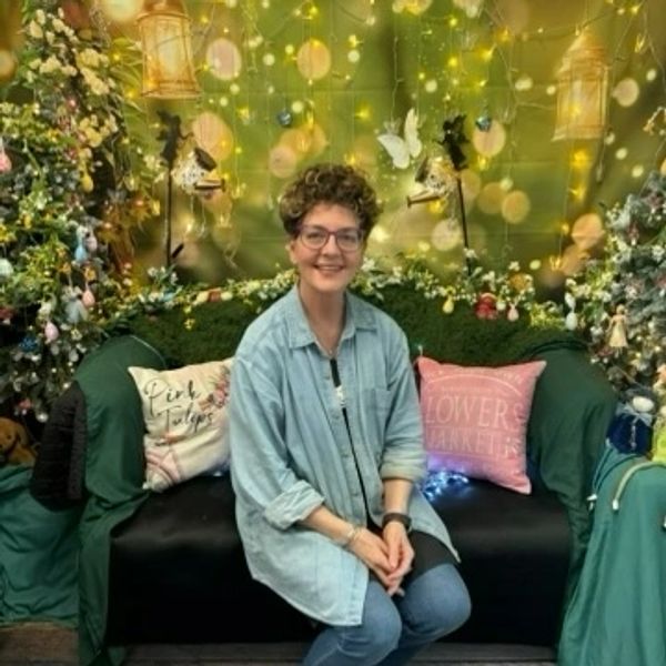 Woman sitting on a decorated couch with fairy lights and flowers.
