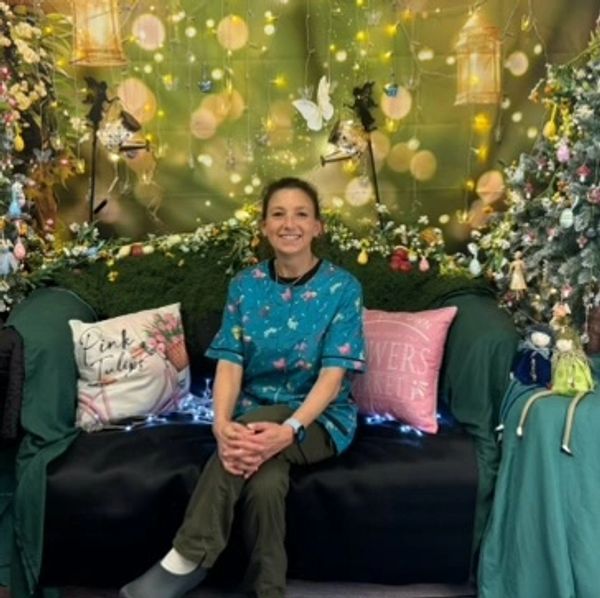 Woman smiling on a decorated couch with floral cushions and fairy lights.