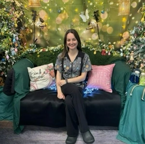 Young woman smiling on a decorated couch with floral and fairy lights.