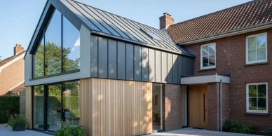 Modern house extension with glass and wood accents beside traditional brick home.