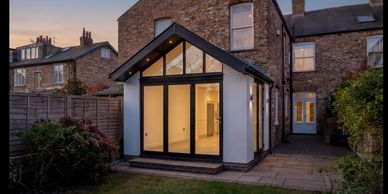 Modern glass extension on a brick house at dusk.