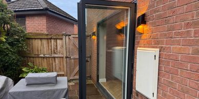 Open glass door reveals outdoor patio area with covered furniture.
