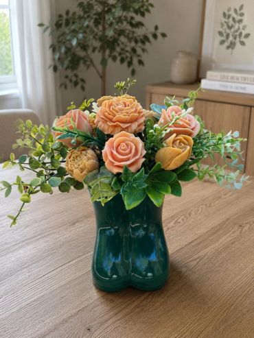 Peach roses and greenery in a green boot-shaped vase.