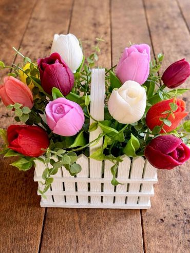 Colorful tulips in a small white basket on wooden surface.