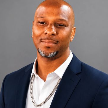 Confident man in a navy blue suit and white shirt with a silver chain.