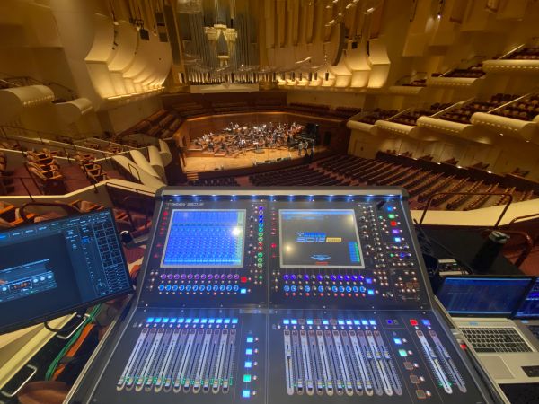 Sound mixing console in a concert hall with orchestra on stage.