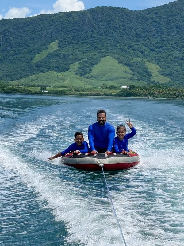 Three people enjoying tubing on a lake with a lush green mountain backdrop.