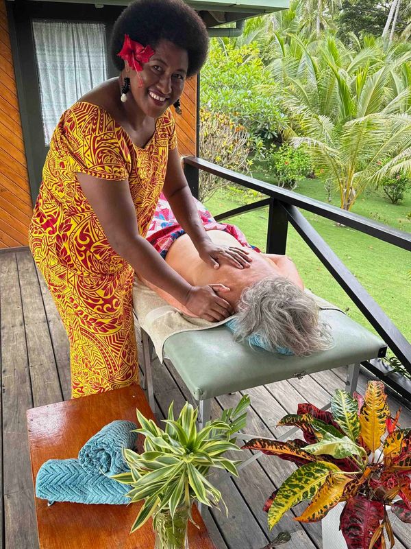 A smiling woman in vibrant dress giving an outdoor massage on a wooden deck.