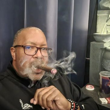 Man smoking a cigar with smoke swirling around him indoors.
