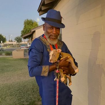 Man in blue traditional attire holding a small brown and white puppy.