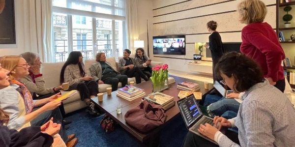 Group of people in a cozy living room with a virtual meeting on TV.