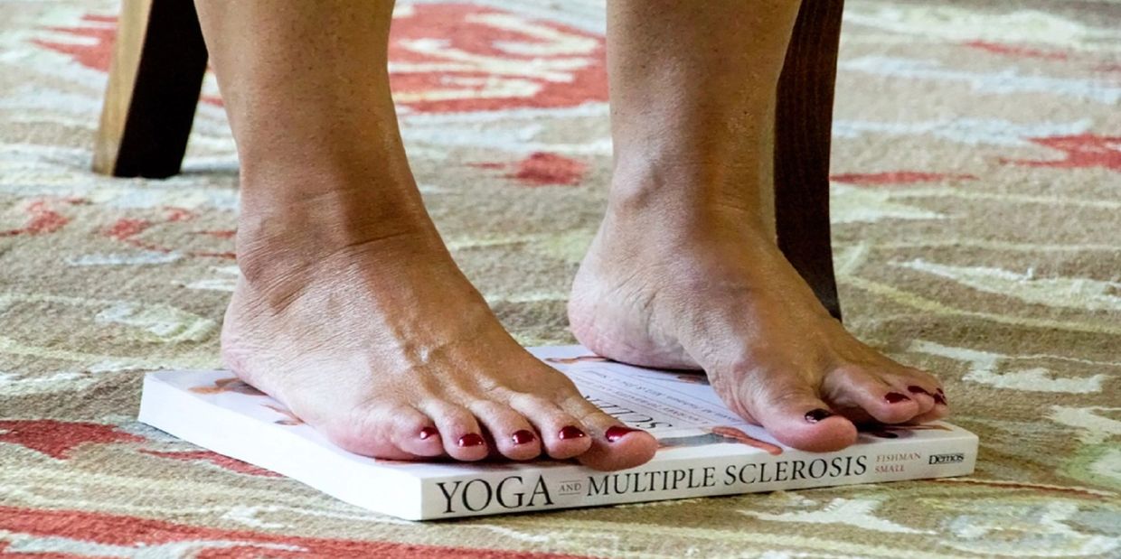 Pair of bare feet on top of a book on the floor titled 'YOGA and Multiple Sclerosis'