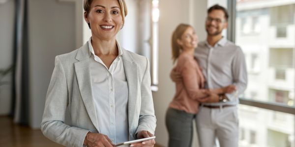 Confident businesswoman holding a tablet with a happy couple in the background.