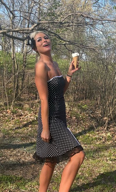Woman in a black polka dot dress holding an ice cream cone outdoors.