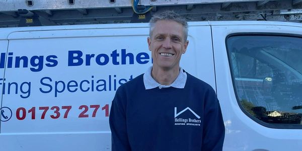 Man in work uniform standing in front of a roofing company van.