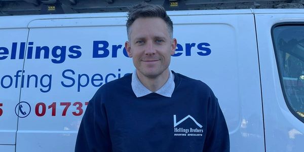 Man in a roofing specialist sweatshirt standing in front of a company van.