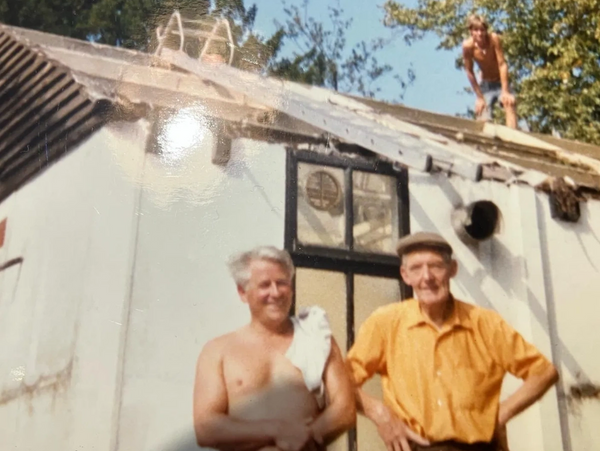 Three men working on a roof and standing in front of a house on a sunny day.