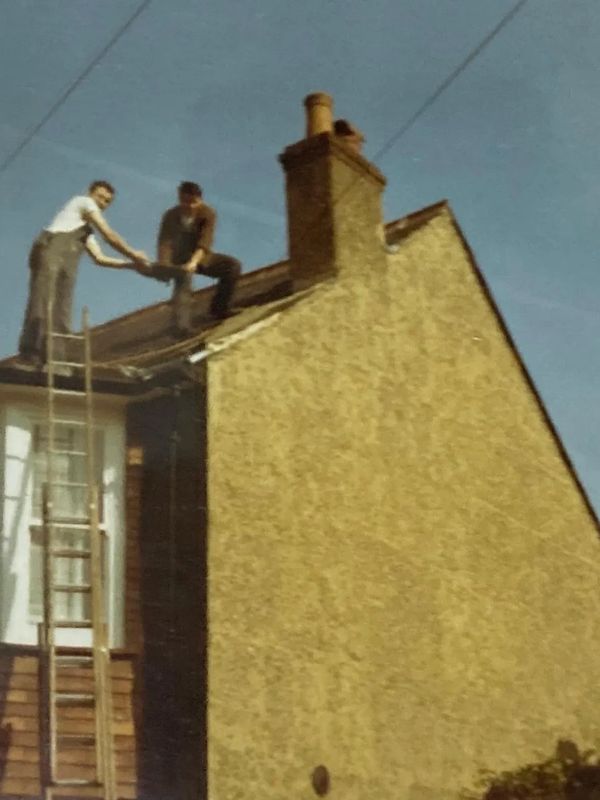 Two men working on a rooftop with a ladder on a sunny day.