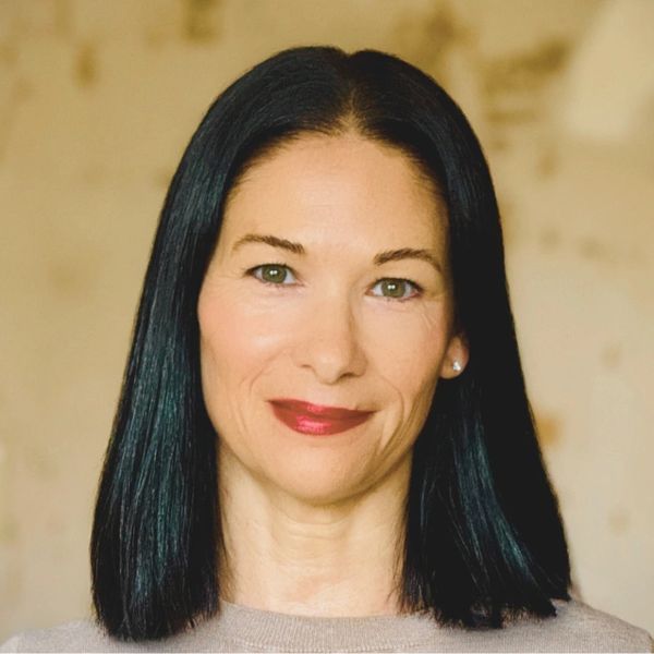 Headshot of Angie Barker. Shoulder length dark hair, tan background.