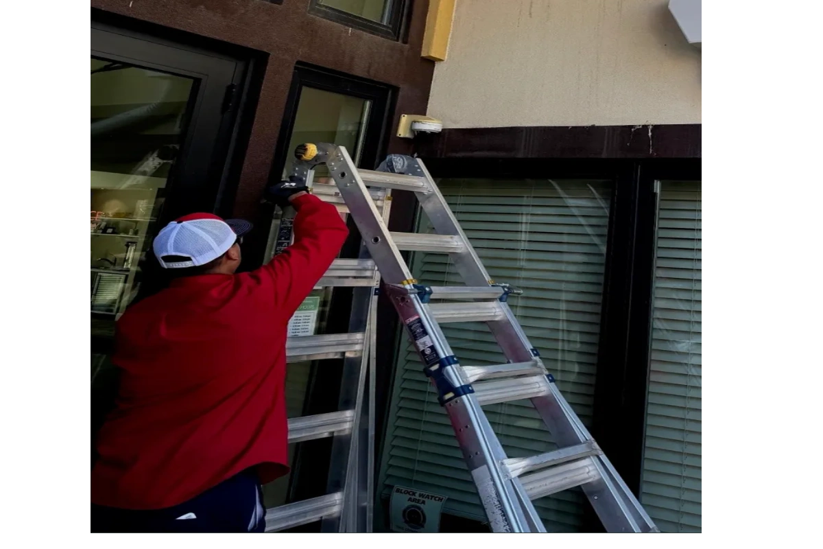 Man in red working on ladder near building.