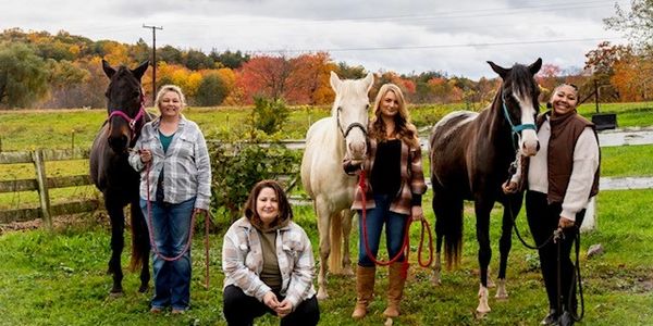 Four women with three horses in a scenic autumn field.