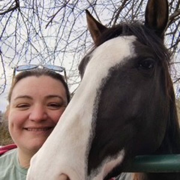 A woman smiling next to a black and white horse.