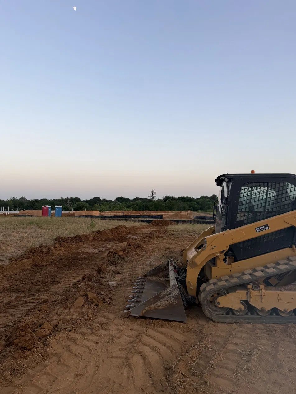 A bulldozer working on a dirt field under a clear sky with a visible moon.