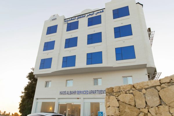 Modern white building with blue windows labeled Hams Al Bahr Serviced Apartment.