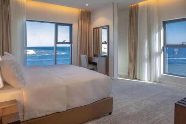Bright hotel room with ocean views through large windows.