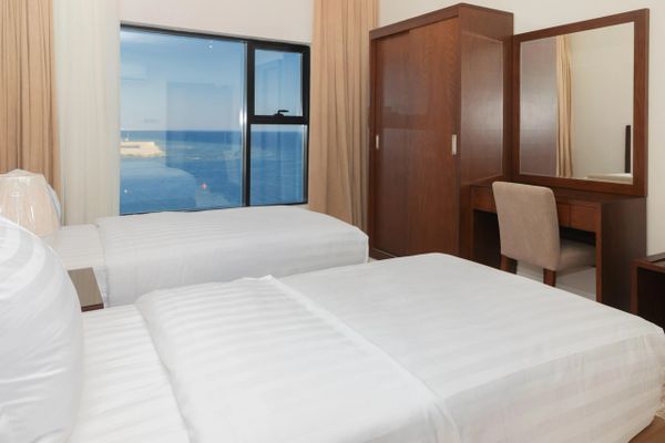 Bright hotel room with twin beds and ocean view through large window.