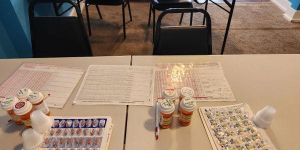 Tables with medication bottles, blister packs, and medical forms in a clinical setting.