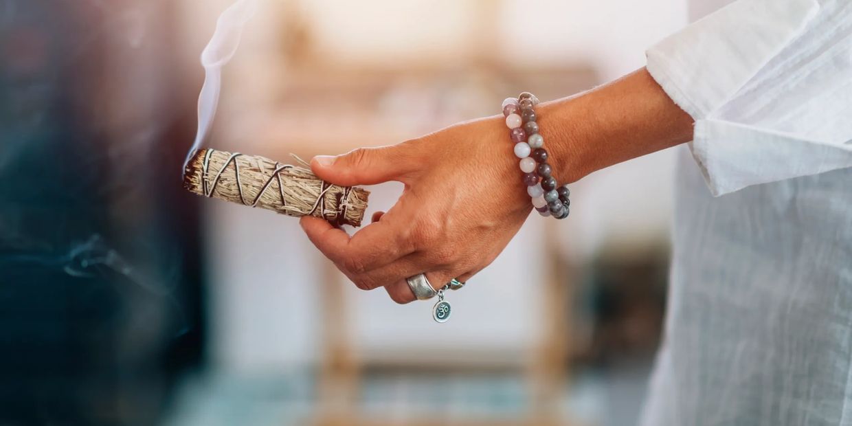 Hand holding a smoldering sage bundle for cleansing or meditation.