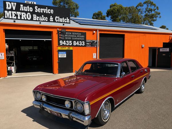 Classic maroon car parked outside auto service shop.