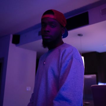 Man in a red cap and gray sweatshirt in moody purple lighting indoors.