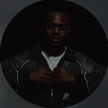 Man adjusting jacket in dim lighting with a serious expression.