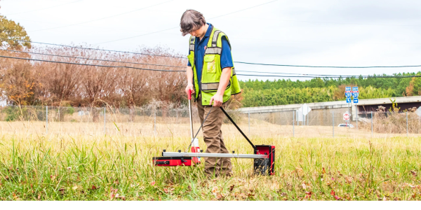 Person using surveying equipment in a field.