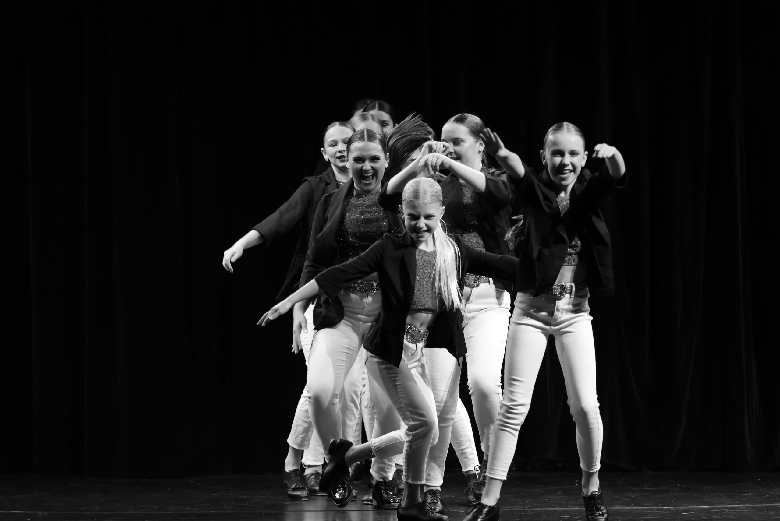 A lively group of young dancers performing on stage in coordinated outfits.