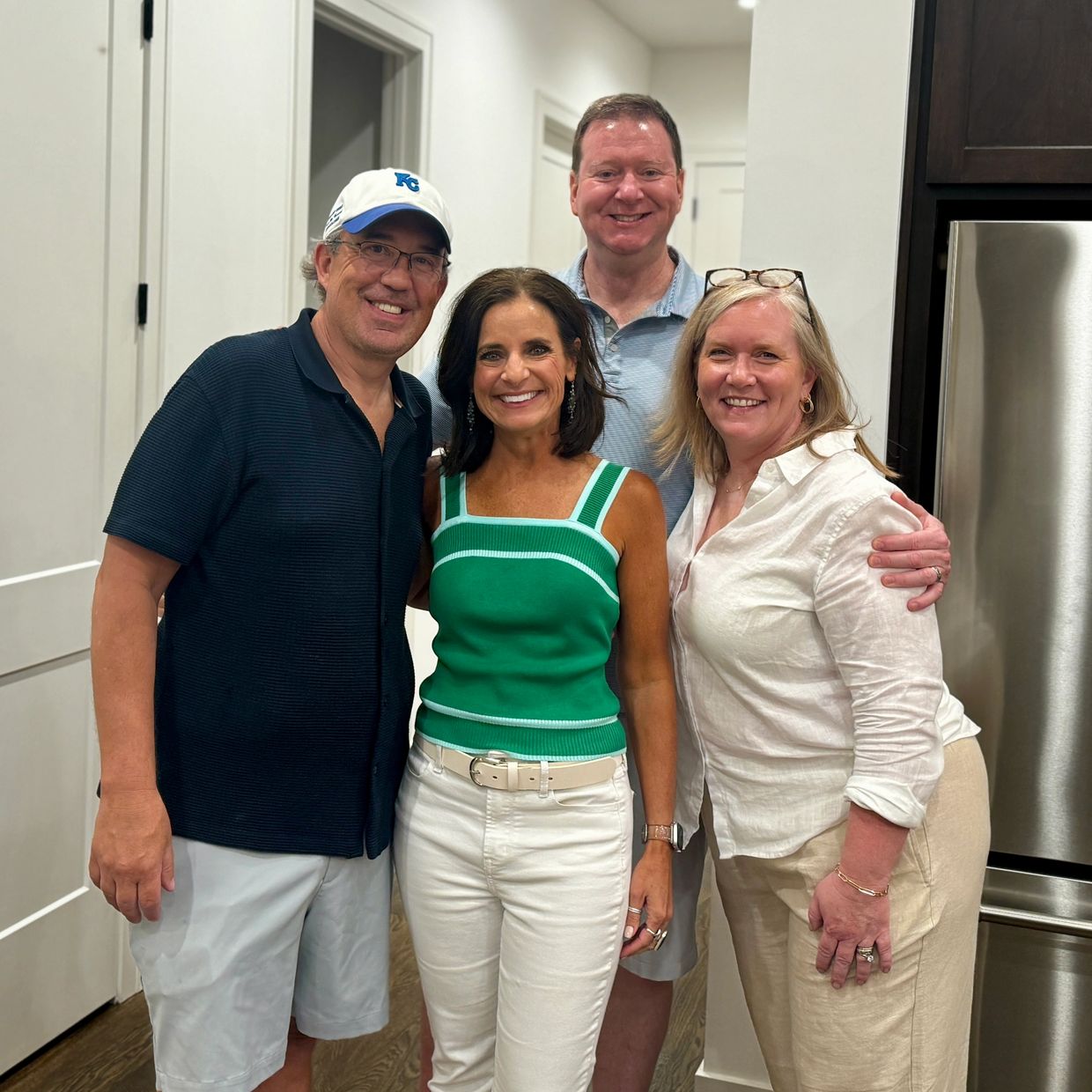 Four friends smiling together indoors in casual summer outfits.