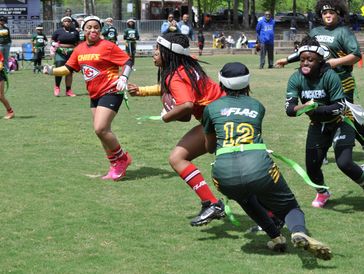 Girls playing flag football on a grassy field.