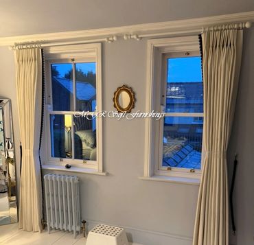 Two windows with cream curtains and a radiator below one window.