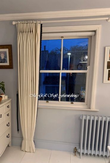 Elegant pleated cream curtain beside a white window and radiator.