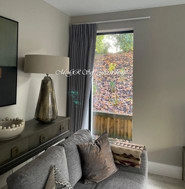 Cozy living room corner with gray sofa, patterned pillows, and a large lamp near a window.