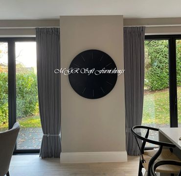 Modern black wall clock centered between two glass doors with curtains.
