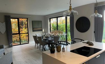 Modern dining and kitchen area with large windows and autumn view.